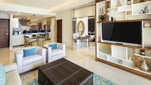 A modern living room with a flat-screen TV, white sofas, a coffee table, and a bookshelf with decorative items. - Modern 1-bedroom hotel suites in charming Cancun  Mexico (Cabo San Lucas)