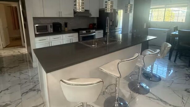 A modern kitchen with white cabinets, a marble countertop, and a central island with bar stools. - 3-bedroom house in enchanting in  LA with AC  fitness area and swimming pool (Los Angeles)