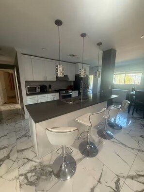 A modern kitchen with white cabinets, a marble countertop, and a central island with bar stools. - 3-bedroom house in enchanting in  LA with AC  fitness area and swimming pool (Los Angeles)