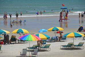 A beach with multiple umbrellas and chairs, a lifeguard tower, and people in the water. - Ocean Walk Resort - 1 BD w/ Balcony April 8-12th (Daytona Beach)