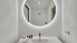 Un baño moderno con un espejo redondo, un lavabo blanco y una ducha.