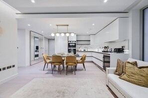 Eine moderne Küche mit weißen Schränken, einem Essbereich mit rundem Tisch und Stühlen sowie einer Couch mit Zierkissen.