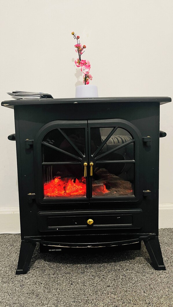 A black wood-burning stove with a glass door and a pink flower on top. - 3 Bedrooms Apartment Self Check In Free Parking (Cowdenbeath)