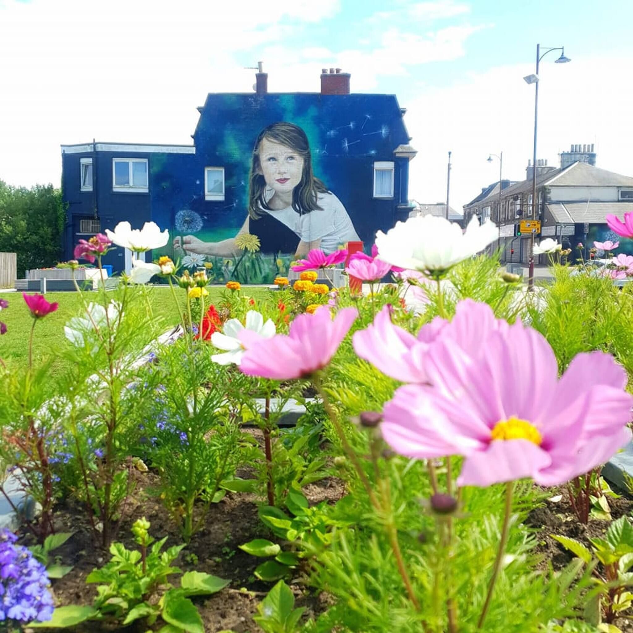 Un jardín con diversas flores y un mural en una edificación al fondo.