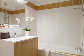Een moderne badkamer met een witte wastafel, een houten kastje, twee witte orchideeën en een bad.