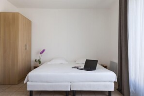 Et moderne hotelværelse med en stor seng, et træskab, et lille natbord med en bærbar computer og en orkidé i potte.