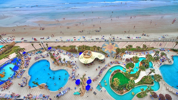 Un complejo turístico con varias piscinas, una zona de playa y sillones de descanso.