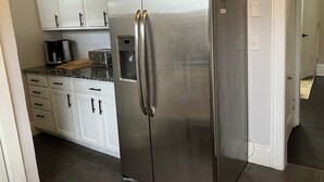 A kitchen with white cabinets, a stainless steel refrigerator, a coffee maker, and a toaster. - Bold 1922 Designer Home - 3BR Near German Village (Columbus)