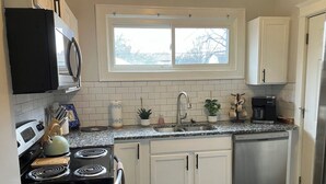 A kitchen with white cabinets, a black stove, a stainless steel sink, a window above the sink, and a coffee maker. - Bold 1922 Designer Home - 3BR Near German Village (Columbus)