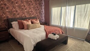 A bedroom with a large bed, a nightstand, a bench, and a window with curtains. - Bold 1922 Designer Home - 3BR Near German Village (Columbus)