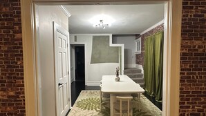 A narrow hallway with a white door on the left, a white table with two chairs, and a green patterned rug. - Bold 1922 Designer Home - 3BR Near German Village (Columbus)