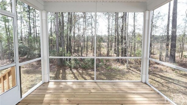A covered porch with a wooden floor and large windows offering a view of a forested area. - The Beautiful and Spacious Big House in Savannah GA (Savannah)