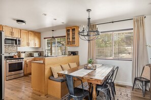 A modern kitchen with wooden cabinets, a built-in oven, a microwave, and a dining area with a wooden table and chairs. - Timberlake Chalet | FIFA Ready! (Lake Arrowhead)