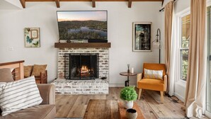 A living room with a fireplace, a sofa, a chair, a television, and a window with curtains.