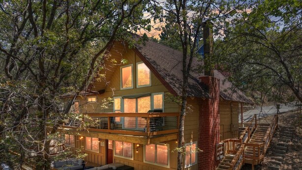 A two-story wooden cabin with a balcony, a fireplace, and a deck with outdoor seating.