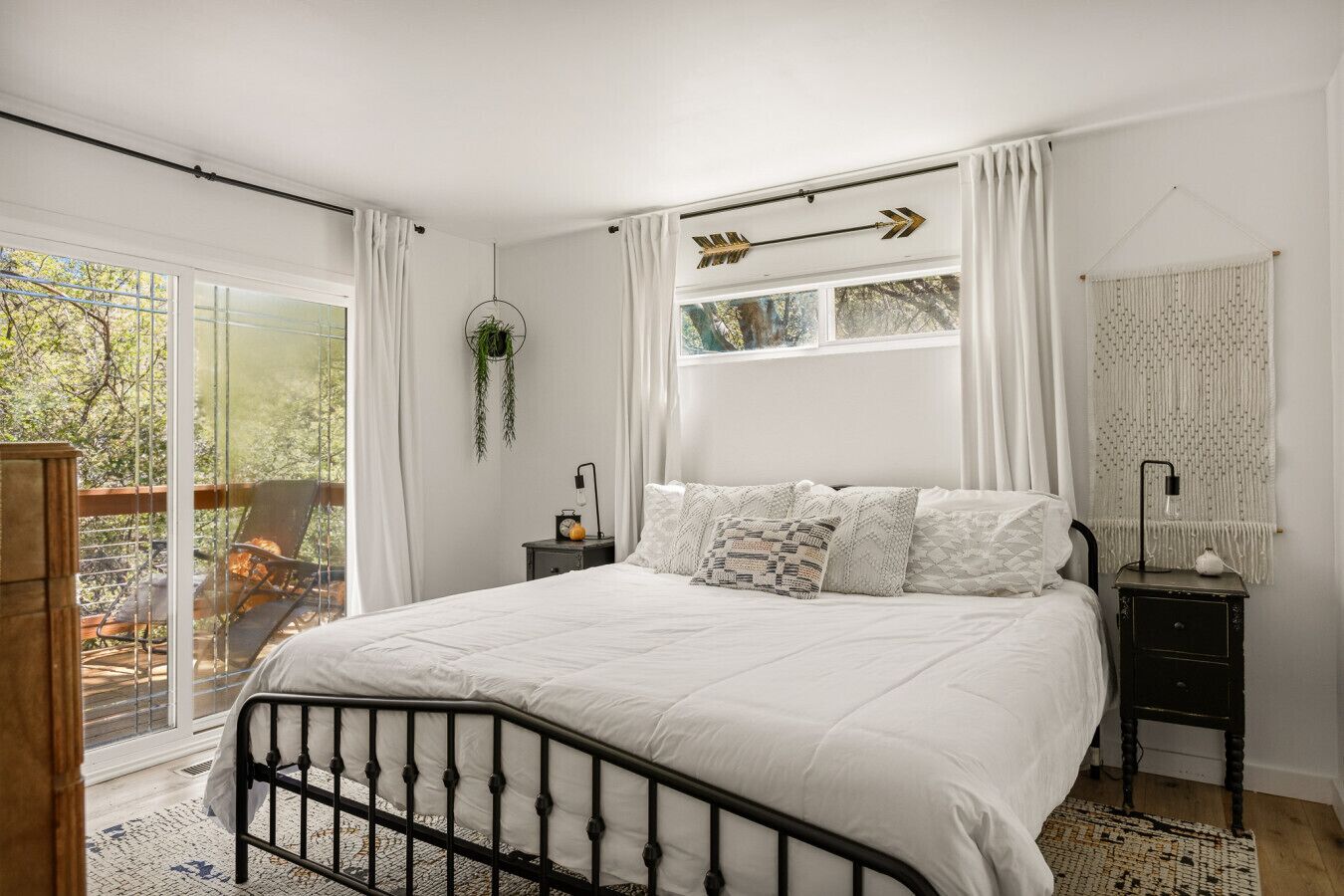 Ein Schlafzimmer mit einem Bett, einem Nachttisch, einer hängenden Pflanze und Blick ins Freie.