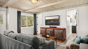 A living room with a grey sofa, a wooden cabinet, a television, and a view of a lake through a window.