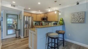 A modern kitchen with wooden cabinets, stainless steel appliances, and a bar area with stools. - Pet Friendly, St. Pete Beach Condo w/AC, 1BR+Sofa Bed, Steps to Beach! (St. Pete Beach)