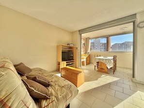 A bedroom with a bed, a TV, a wooden cabinet, a dining table, and a view of the outside. - CAP D'AGDE - Plage Richelieu // Réf 0163 (CAP D'AGDE)