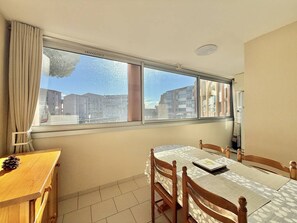 Un coin repas avec une table et des chaises, une fenêtre avec des rideaux et une vue sur les bâtiments à l’extérieur.