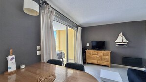 A modern living room with a wooden dining table, a TV on a wooden cabinet, and a sailboat decoration on the wall. - CAP D'AGDE - Plage Richelieu // Réf 0168 (CAP D'AGDE)