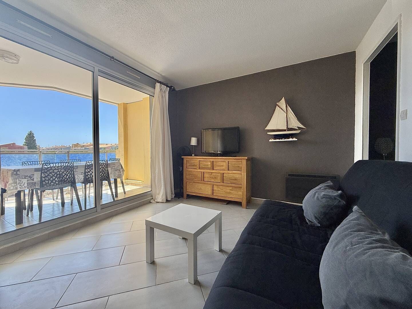Una sala de estar con un sofá, un televisor sobre un mueble de madera y vistas al mar a través de amplios ventanales.