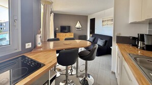 A modern kitchen with a black stove, wooden countertop, and a dining area with a round table and two bar stools. - CAP D'AGDE - Plage Richelieu // Réf 0168 (CAP D'AGDE)
