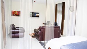A modern hotel room with a bed, a sofa, a massage chair, and a TV on the wall. - Premium HOTEL (Douala)