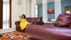 A living room with a brown leather sofa, a patterned rug, and a blue wall with a painting. - Premium HOTEL (Douala)