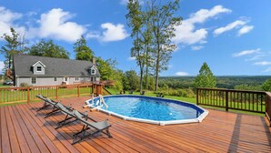 Eine Holzterrasse mit Swimmingpool, Liegestühlen und Blick auf ein Haus und die Landschaft.