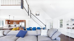 Ein geräumiger Wohnbereich mit einem grauen Ecksofa, einer Treppe und einer Küche im Hintergrund.