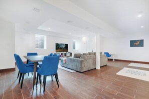 A spacious living area with a dining table, blue chairs, a sofa, and a television. - Kingston Ridge Chalet - Hot Tub & Pool (Kingston)