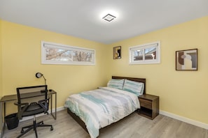 A bedroom with a bed, a desk with a chair, two windows, and a ceiling light.