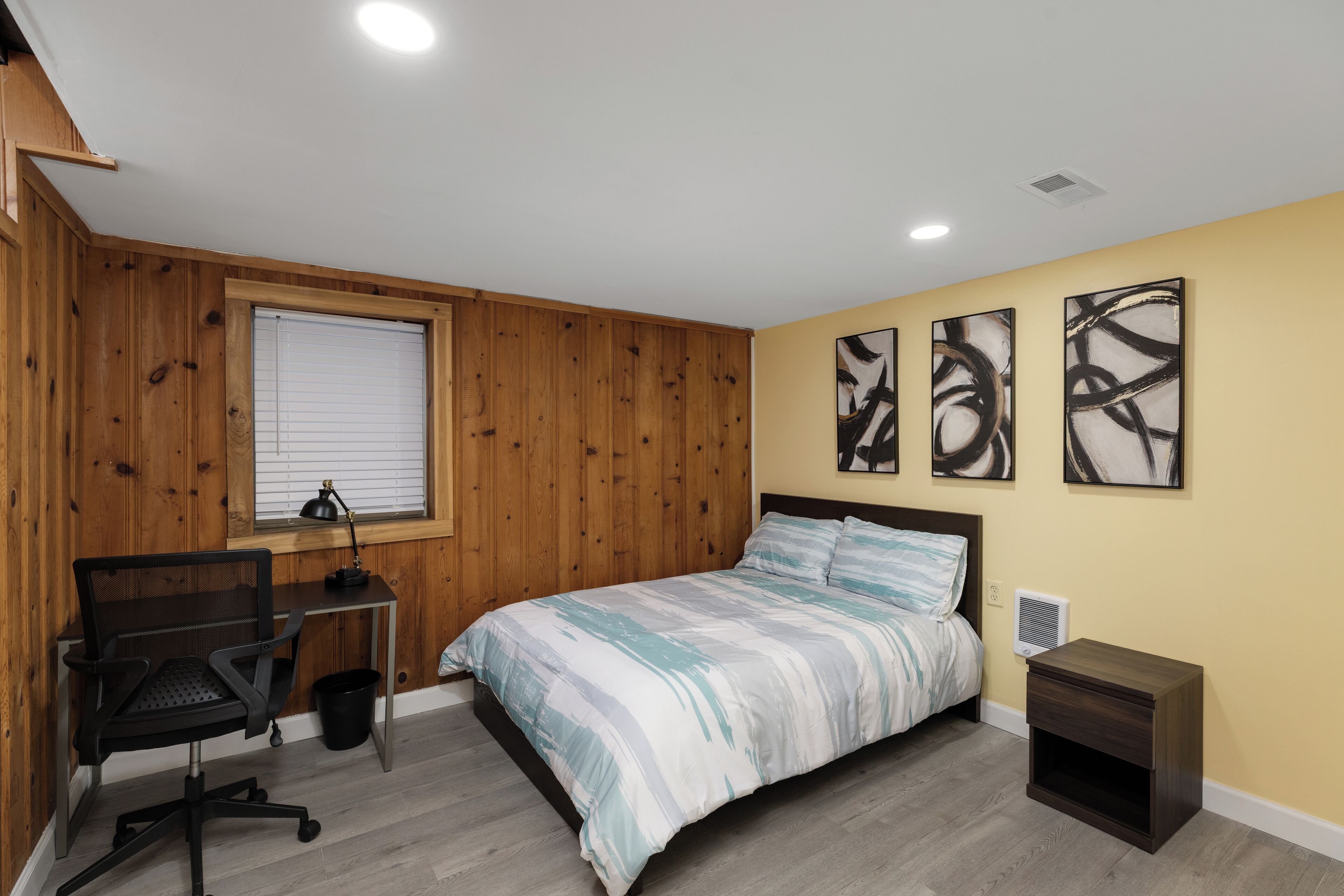 Un dormitorio con cama, un escritorio con silla, una ventana con persianas y una obra de arte en la pared.