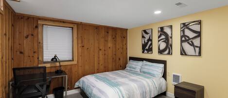 Un dormitorio con cama, un escritorio con silla, una ventana con persianas y una obra de arte en la pared.