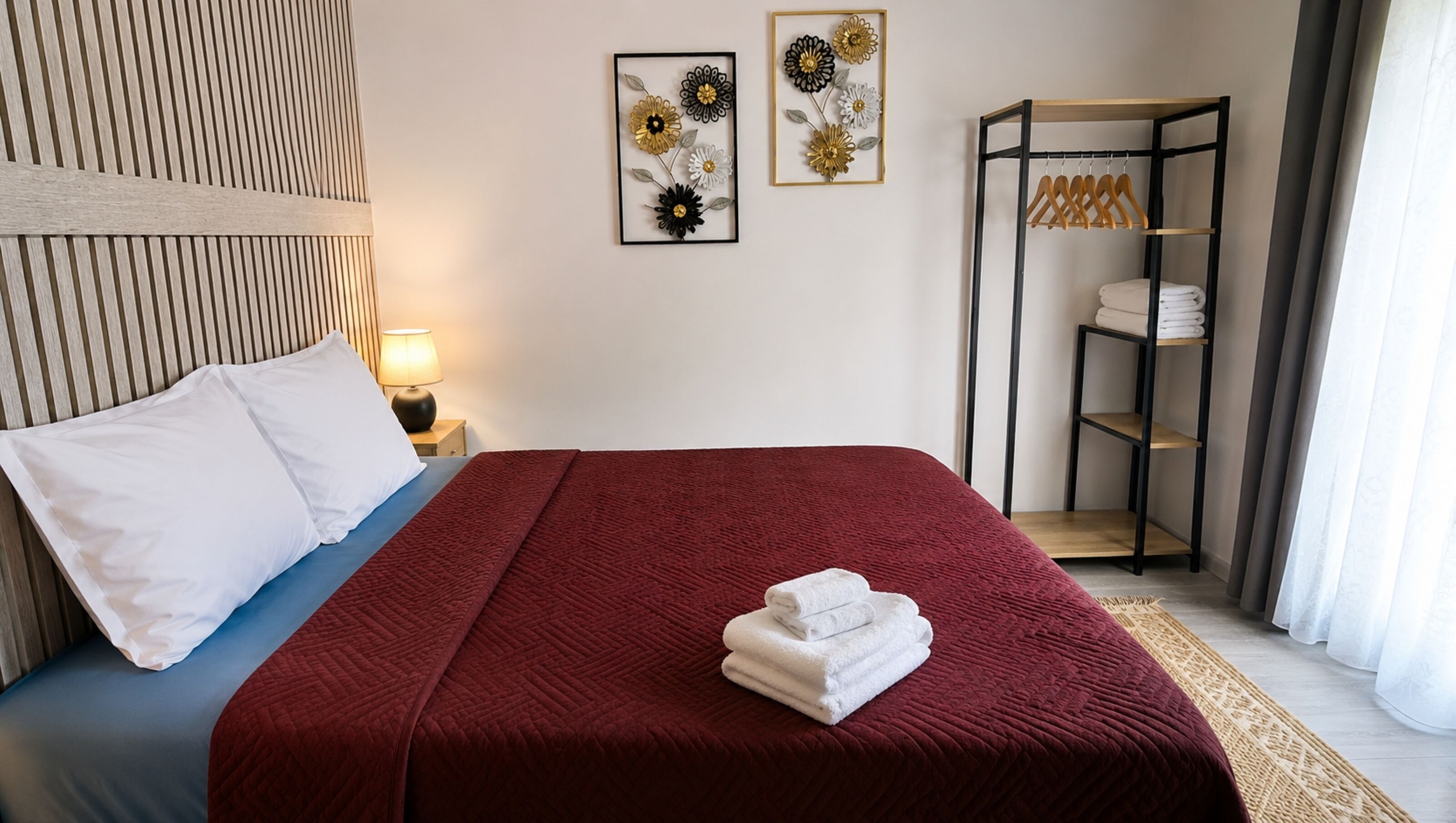 Una camera d'albergo con un letto, un comodino, una lampada, un armadio e due opere d'arte floreali incorniciate appese al muro.