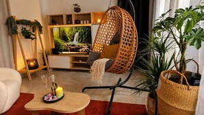Un salon chaleureux avec un fauteuil suspendu, un téléviseur et une grande plante.
