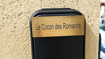 A black object with a brass plaque labeled 'Le Cocon des Romarins' attached to a textured beige wall.