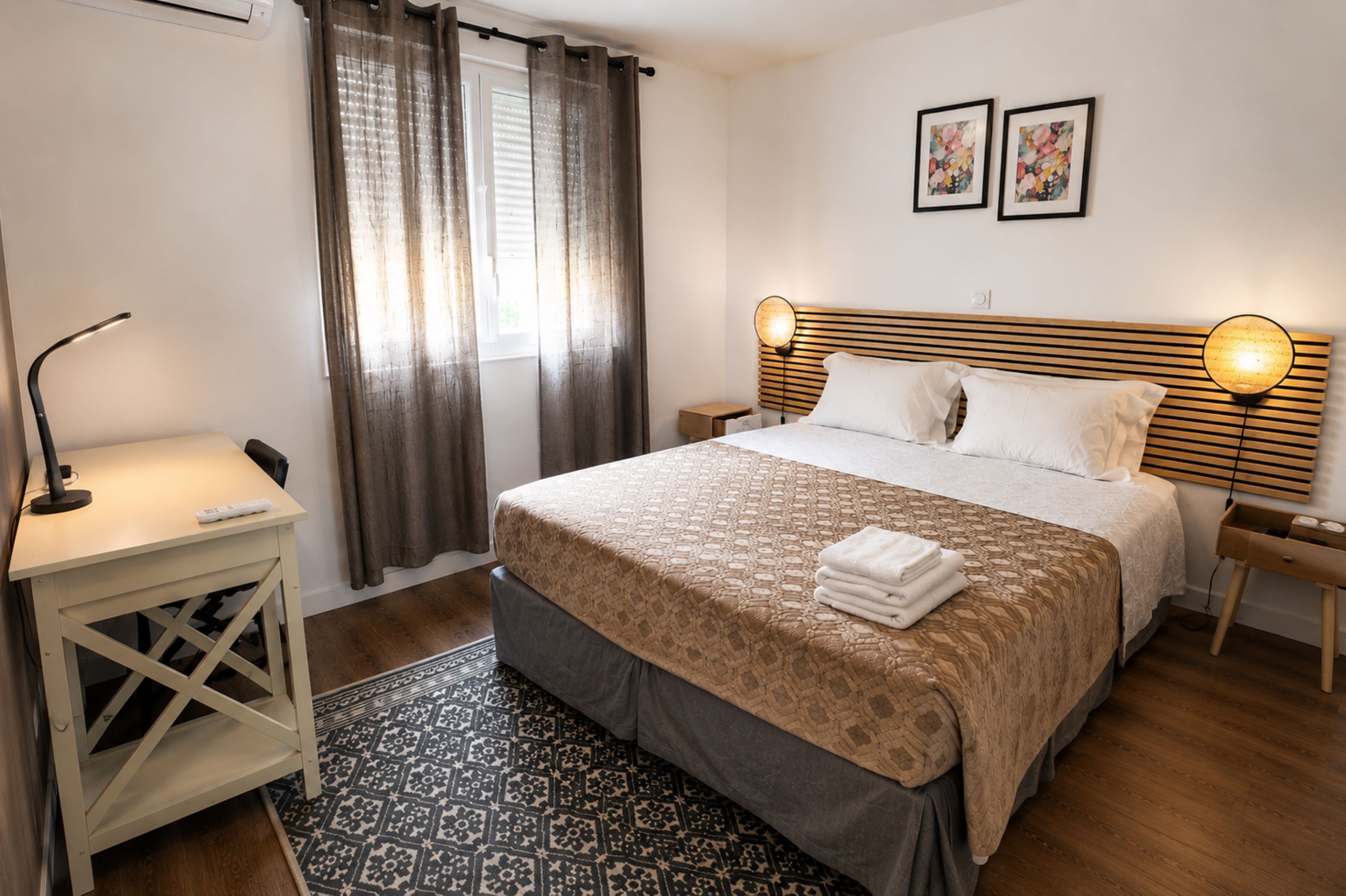 A bedroom with a bed, bedside tables, a desk, a patterned rug, and curtains.