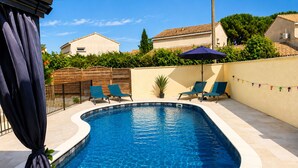 Une piscine avec deux chaises longues, une plante en pot et une clôture en bois.