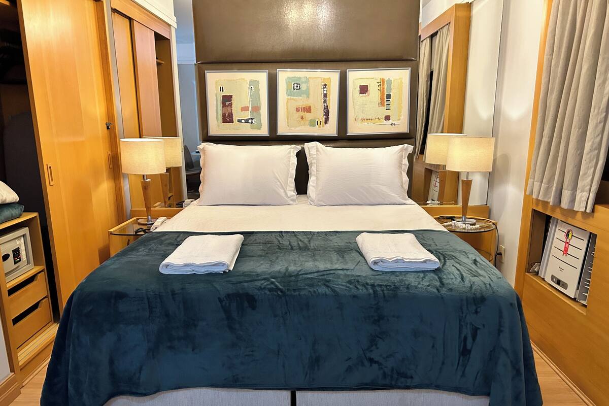 Een hotelkamer met een bed, twee nachtkastjes, een wandtelevisie en kunst boven het bed.
