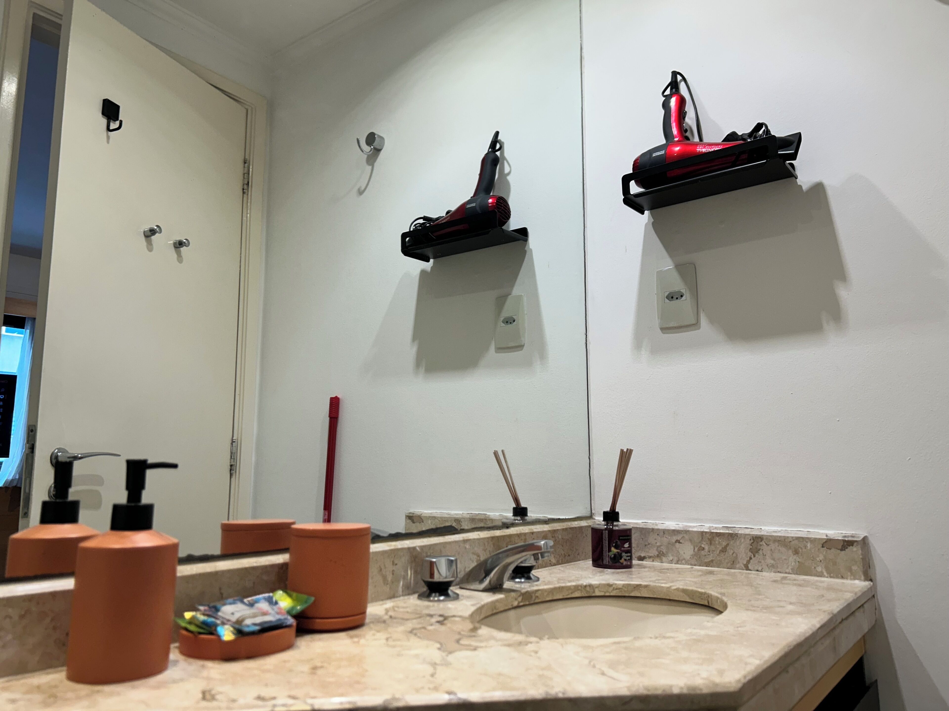 A bathroom with a sink, mirror, and two red hair dryers mounted on the wall.