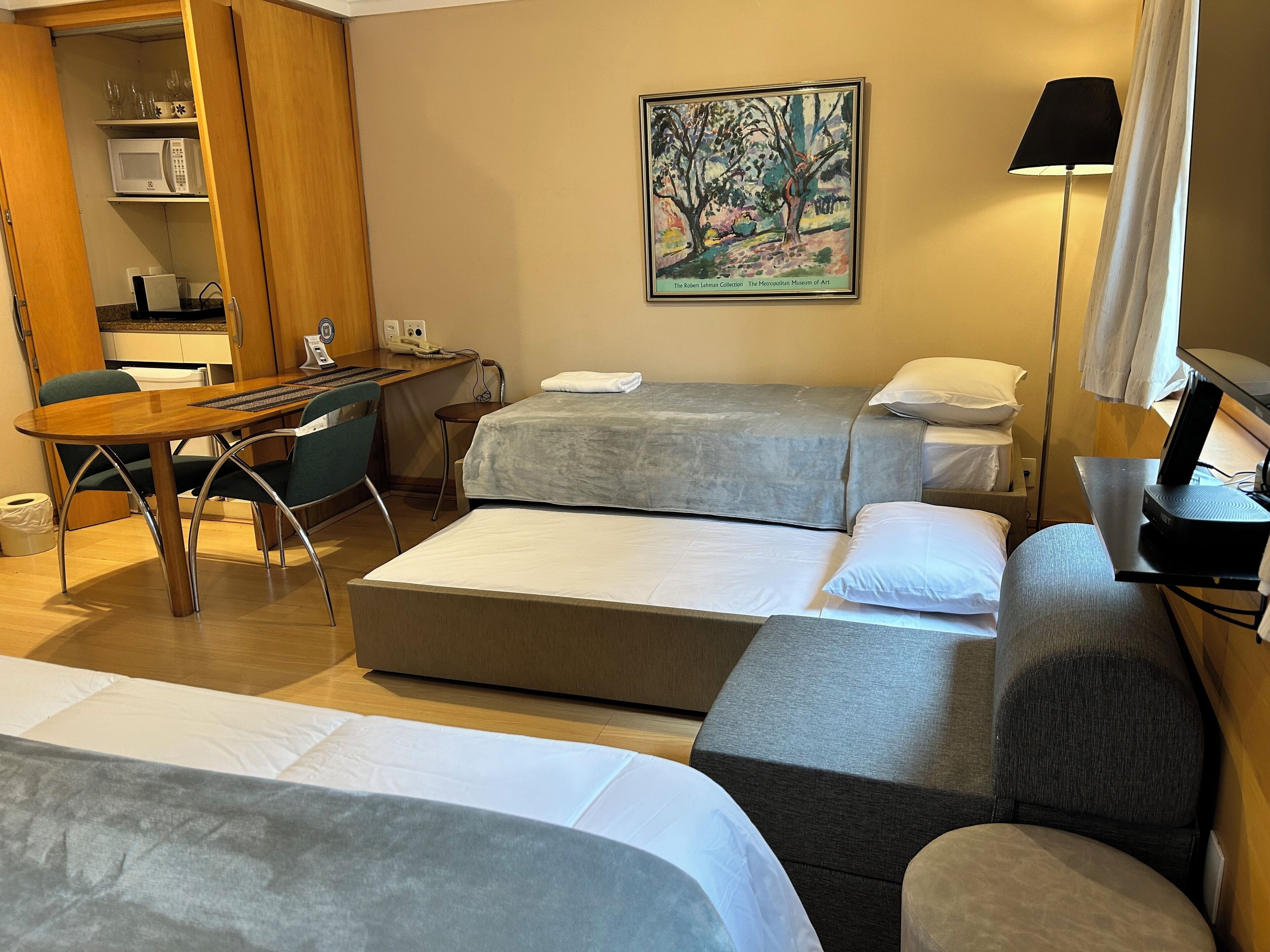 Una camera d'albergo con una scrivania in legno, due letti, un divano, un quadro appeso e una lampada.