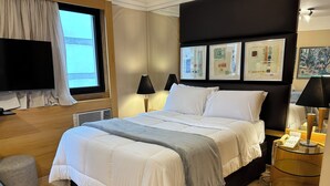Een moderne hotelkamer met een groot bed, een flatscreen televisie, een nachtkastje met een lamp en kunst aan de muur.