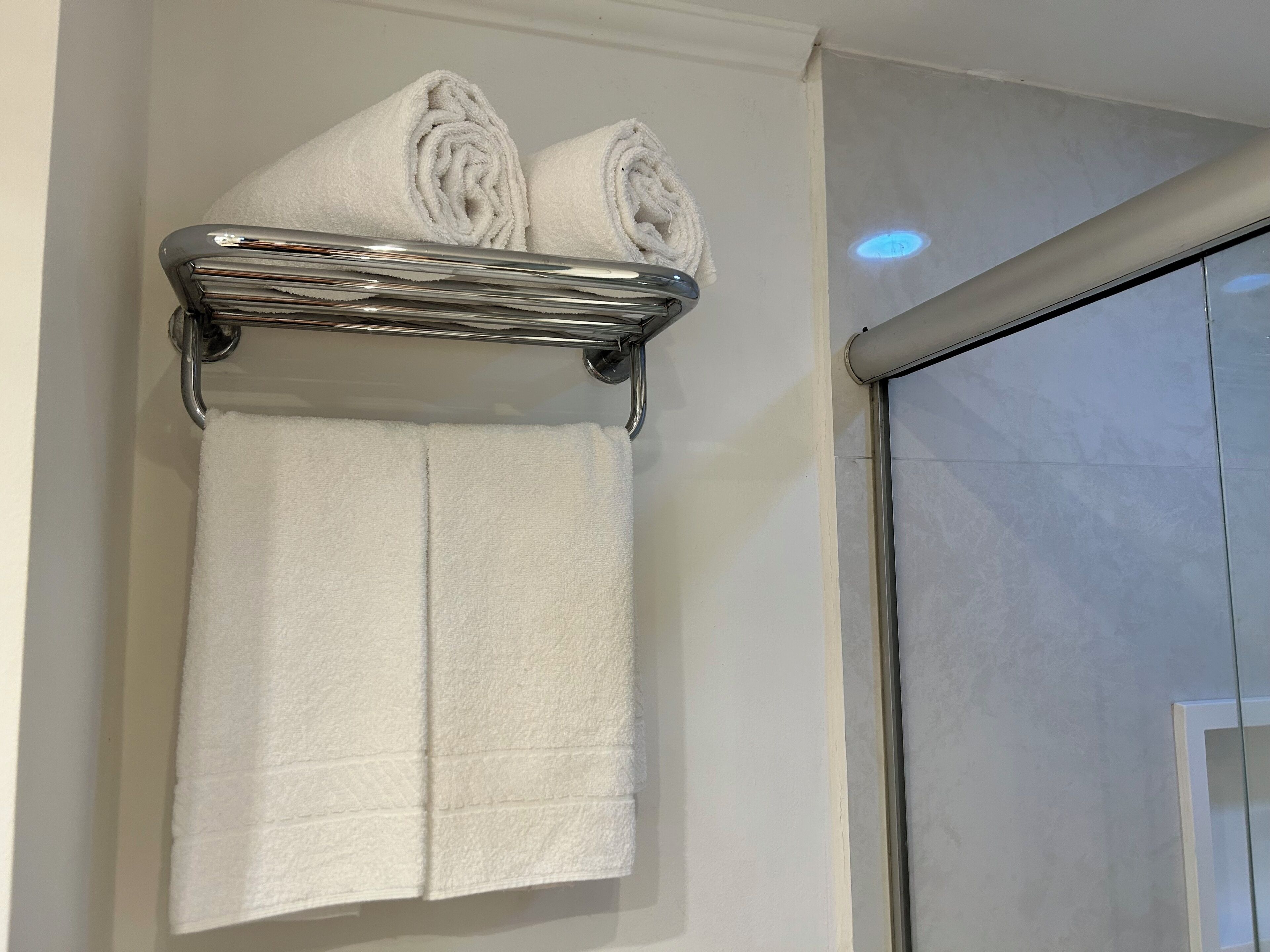 Un baño con un perchero que sostiene dos toallas enrolladas y una sola toalla.