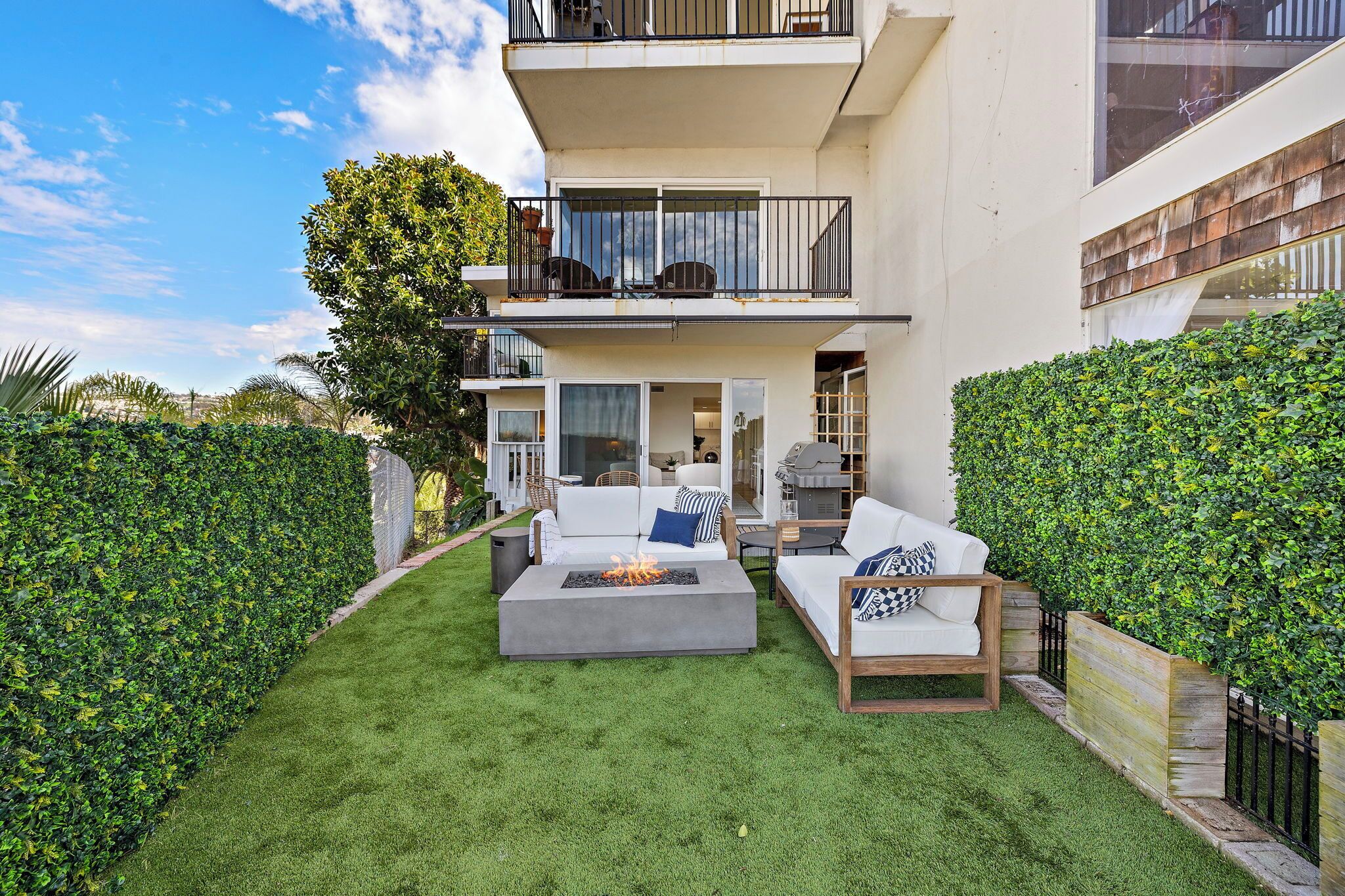 A modern outdoor living area with a fire pit, white sofas, and a wooden table.
