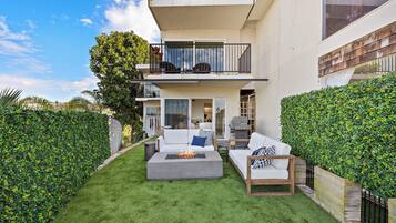 A modern outdoor living area with a fire pit, white sofas, and a wooden table.