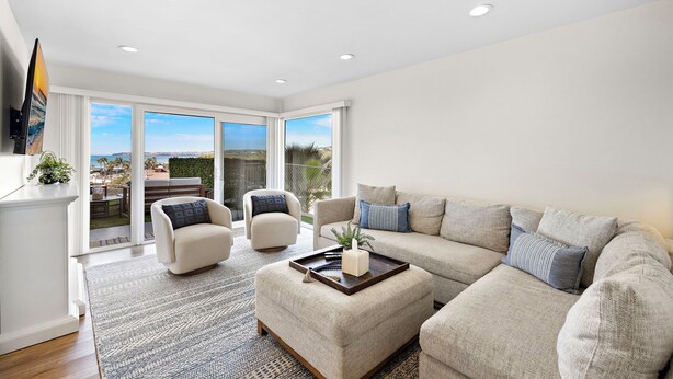 Una sala moderna con un sofá color beige, dos sillones, una mesa de centro y un amplio ventanal corredero que da a un patio exterior.