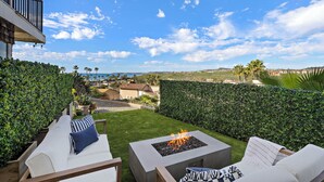 Un patio con un pozo de fuego, asientos al aire libre y vista al océano.