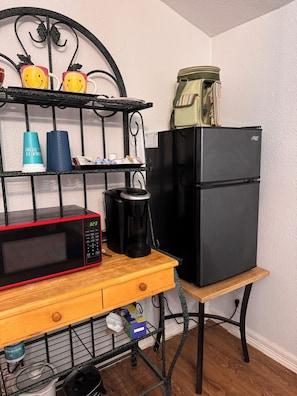 A compact kitchen with a microwave, coffee maker, and refrigerator on a wooden table.